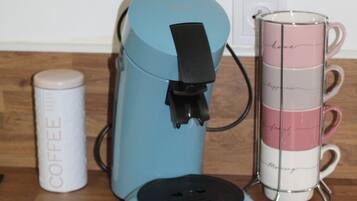 Une machine à café, un porte-tasse et un récipient à café, le tout posé sur un plancher en bois.