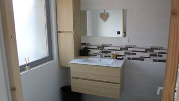 A bathroom with a white sink, wooden cabinets, a mirror with a heart decoration, and a tiled backsplash.