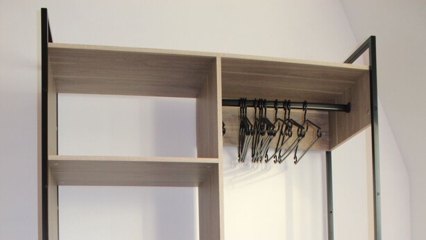 Une armoire en bois dotée de plusieurs étagères et d’une tringle pour suspendre les vêtements, avec un tiroir et un espace pour suspendre les vêtements.