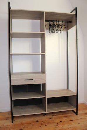 Un armario de madera con varios estantes y barra para colgar, que incluye un cajón y espacio para ropa colgada.