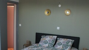 Une chambre à coucher comprenant un lit, une table de chevet, deux appliques murales et une porte donnant sur une autre pièce.
