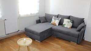 Un salon moderne avec un canapé d’angle gris, une petite table ronde et un radiateur.