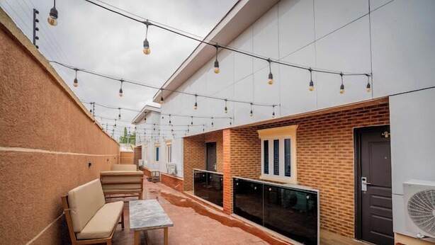 Eine Terrassesituation im Freien mit einer Ziegelwand, einer Holzbank, einem Tisch und Lichterketten.