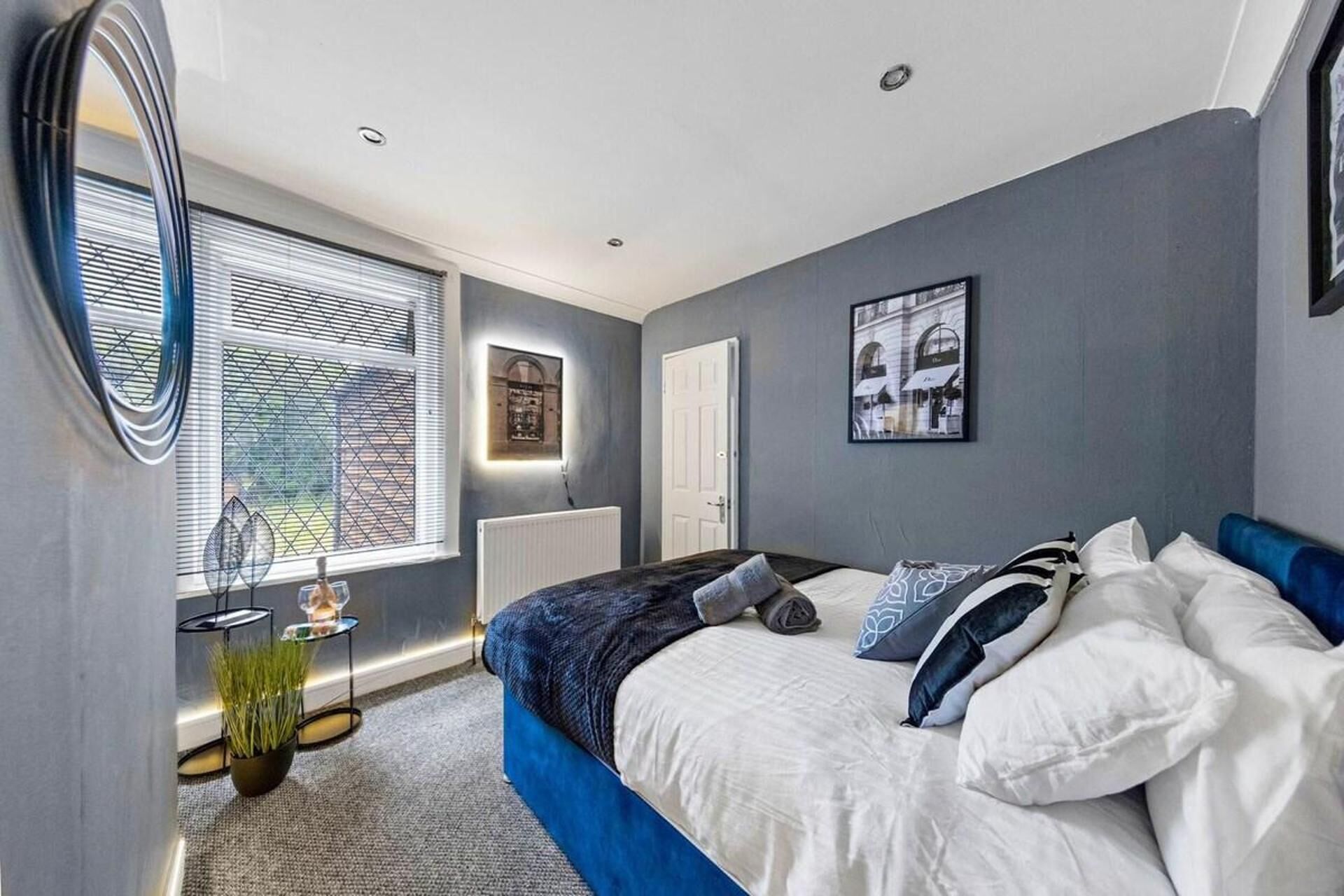 A modern bedroom with a large bed, a radiator, a window with blinds, and a framed picture on the wall.