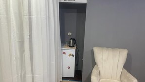 Una habitación con un refrigerador blanco, una silla blanca y una cortina.