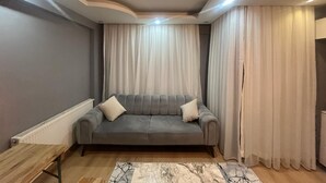 Una sala de estar moderna con un sofá gris, cortinas blancas y una alfombra con diseño de mármol.