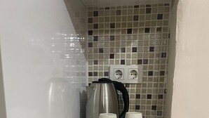 Una encimera de cocina con un hervidor, dos tazas blancas y una tabla de cortar con verduras verdes.