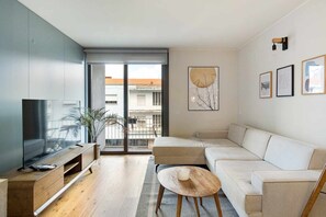 Un salon moderne doté d’un grand téléviseur, d’un canapé, d’une table basse et d’un balcon offrant une vue sur les immeubles.