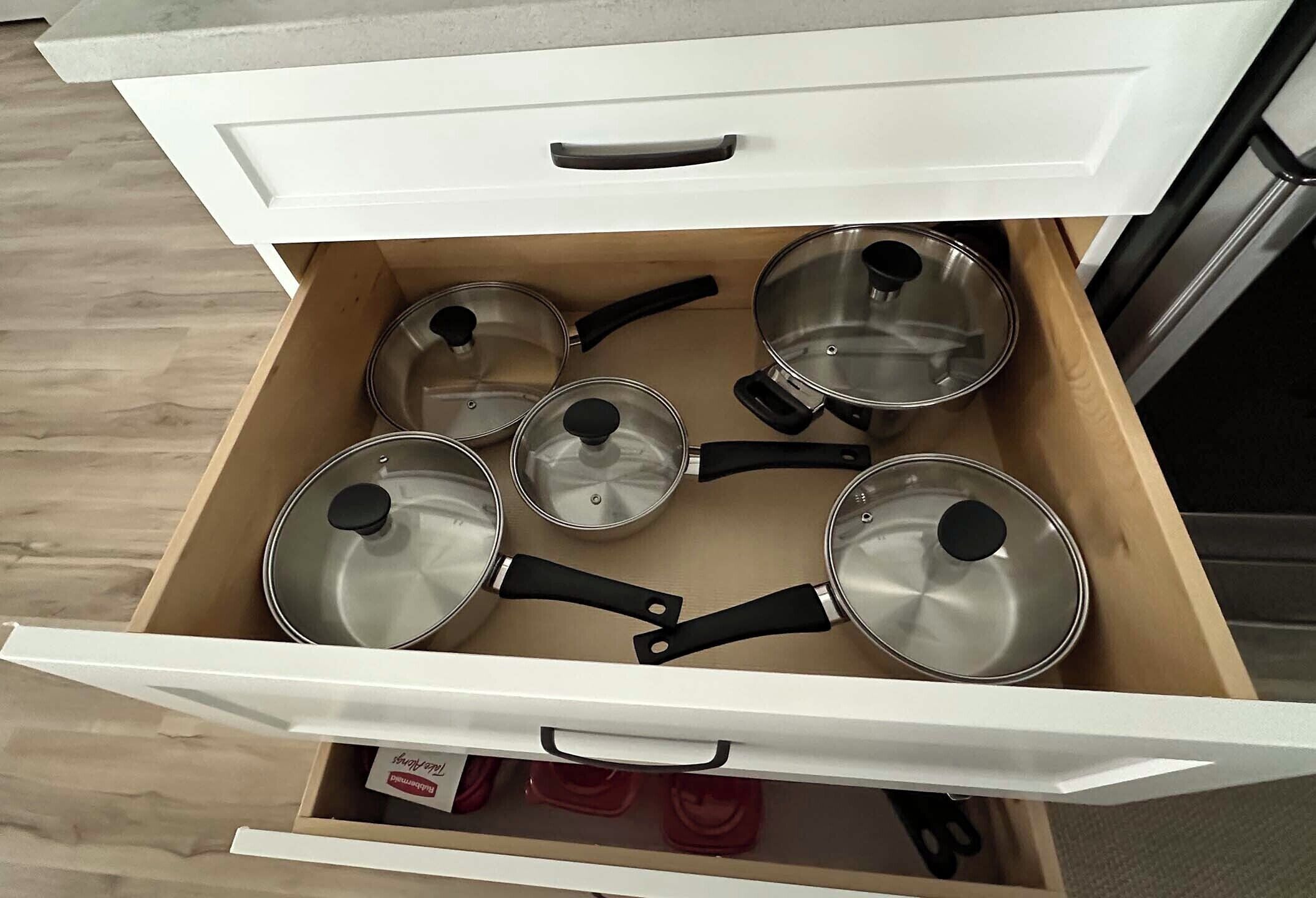 A kitchen drawer with several stainless steel pots and pans.