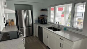 Una cocina moderna con electrodomésticos de acero inoxidable, lavavajillas y una ventana con persianas.