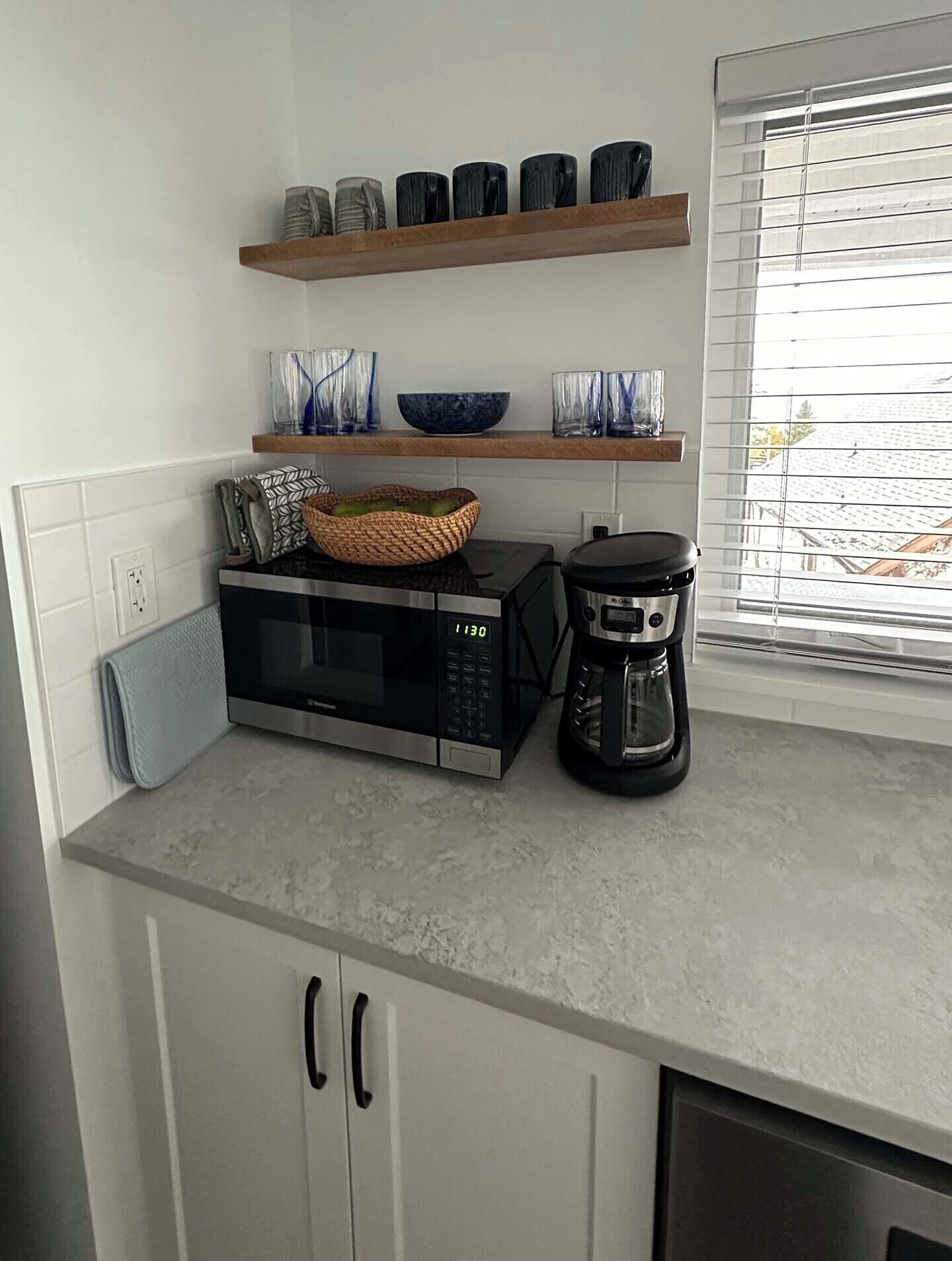 Een keuken met een magnetron, koffiezetapparaat en planken met potten en glazen.