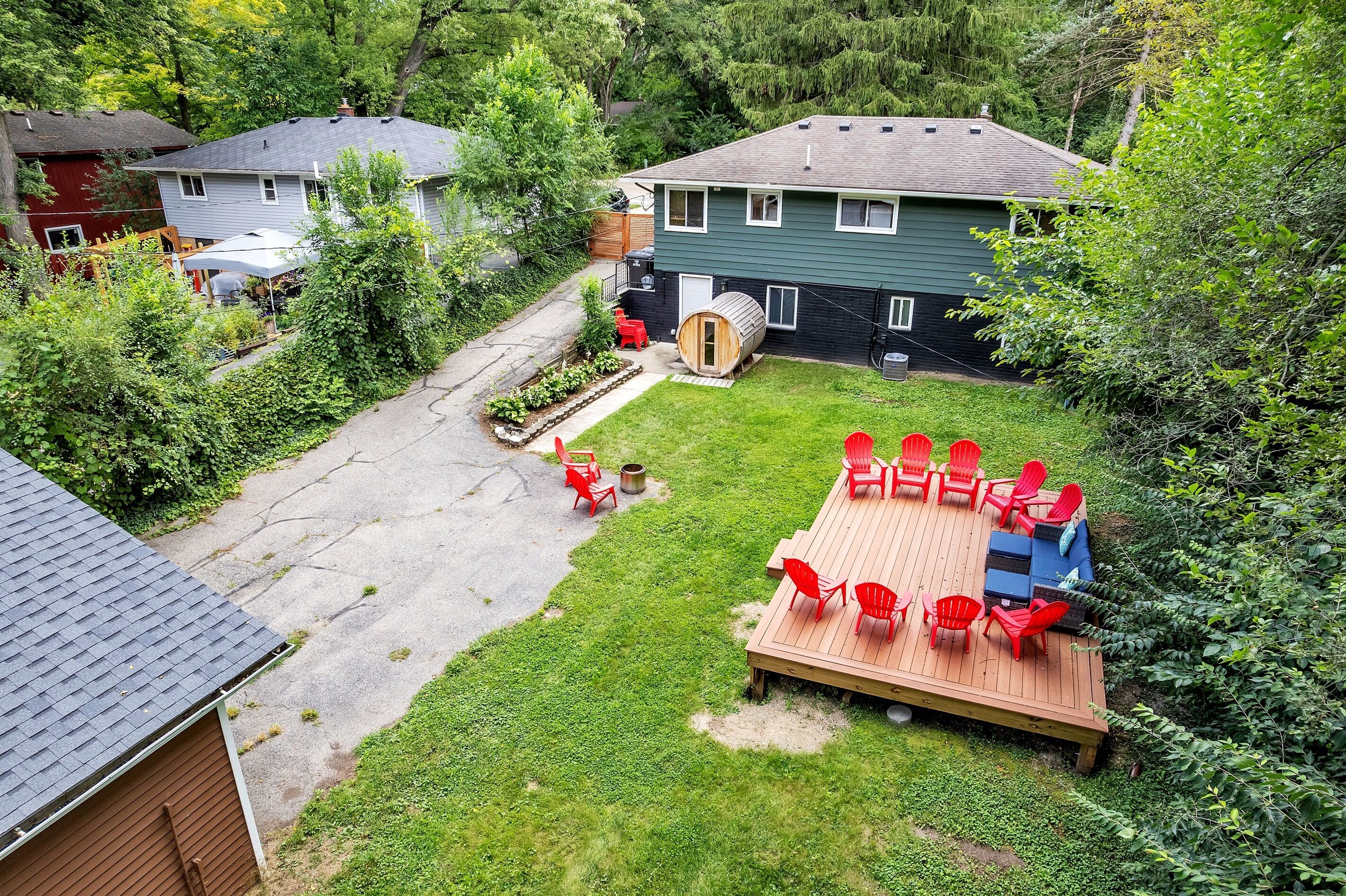 Un jardin avec une terrasse en bois, des chaises rouges et un barbecue.