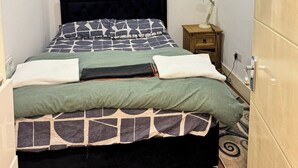 Een net opgemaakt bed met een bedsprei met dessin, een bedlampje en een houten nachtkastje.