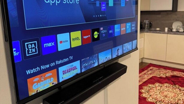 Een flatscreen-tv aan een muur, waarop een interface van een streamingdienst met diverse inhoudsopties wordt weergegeven.