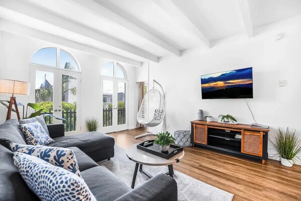 A modern living room with a sofa, a hanging chair, a coffee table, and a TV on the wall.