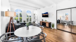 Un salon moderne avec une table à manger ronde, un canapé noir et un téléviseur fixé au mur.