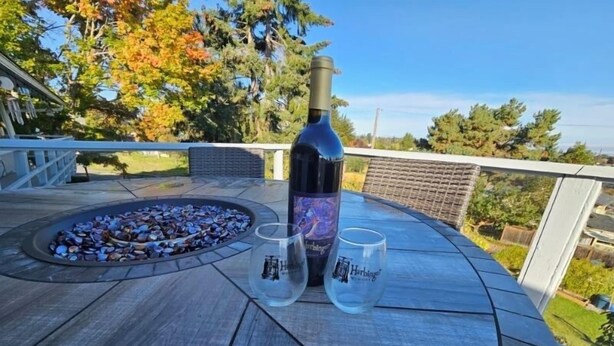 A bottle of wine and two glasses on a wooden deck with a fire pit. - !!NEW!! Water View Oasis (Port Angeles)