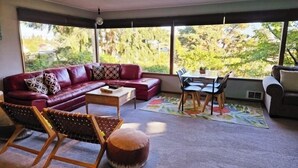 A living room with a red sofa, a wooden coffee table, a dining table with chairs, and a large window offering a view of trees. - !!NEW!! Water View Oasis (Port Angeles)