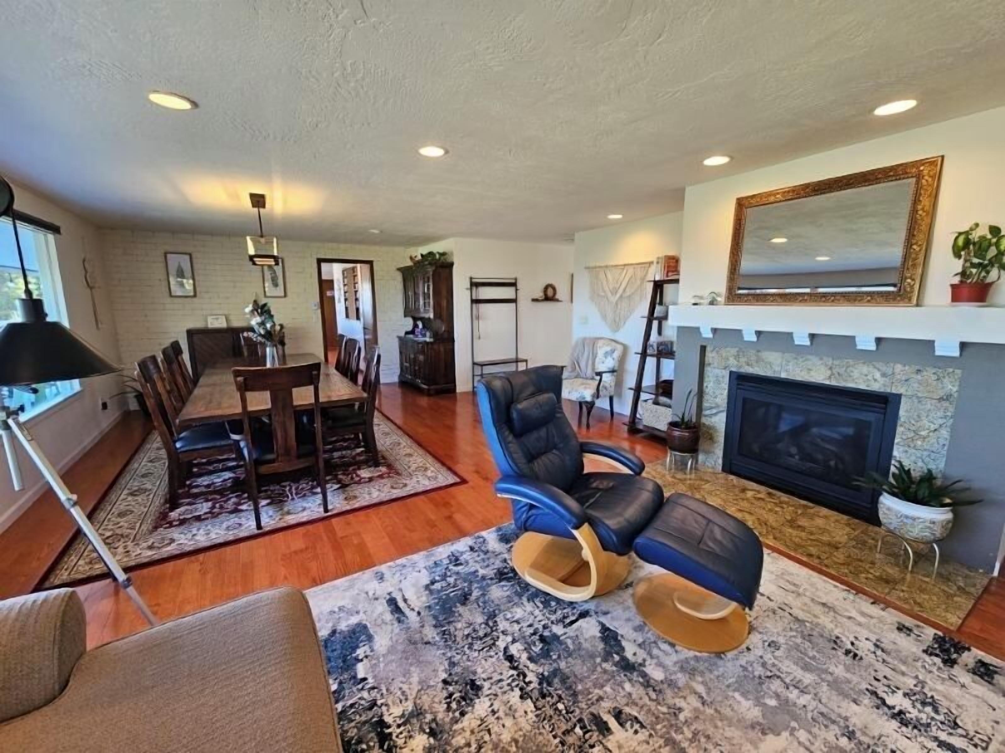 A spacious living room with a fireplace, a dining area with a wooden table and chairs, and a seating area with a blue armchair and a sofa.