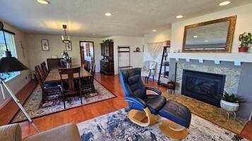 A spacious living room with a fireplace, a dining area with a wooden table and chairs, and a seating area with a blue armchair and a sofa.