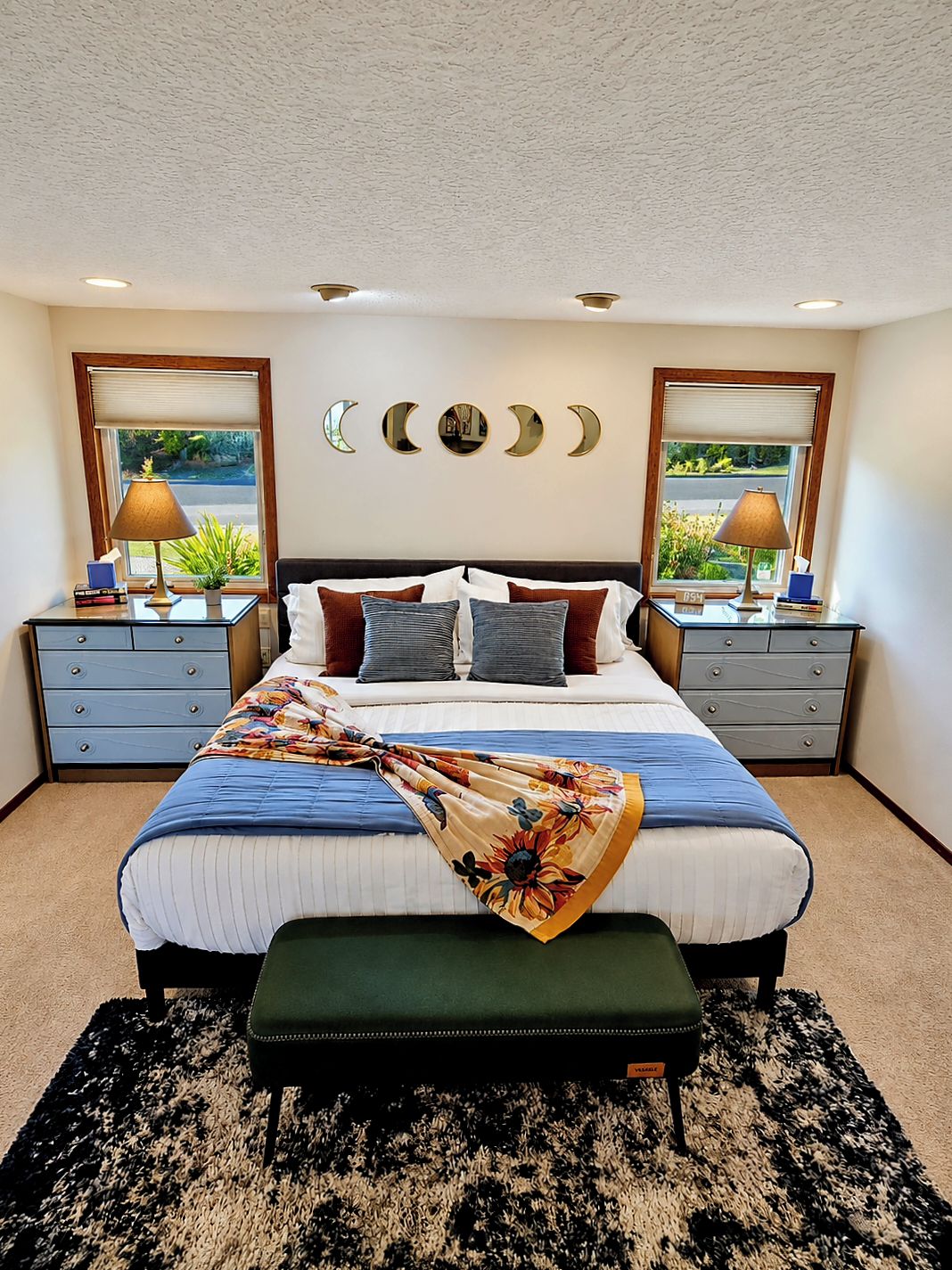 Une chambre à coucher avec un lit, des tables de chevet, des lampes, une horloge et une vue sur l’extérieur.