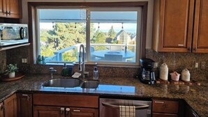 A kitchen with a large window, granite countertops, wooden cabinets, a built-in microwave, and a coffee maker. - !!NEW!! Water View Oasis (Port Angeles)