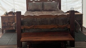 Une tente avec un lit en bois, des tables de chevet en bois et un tapis.