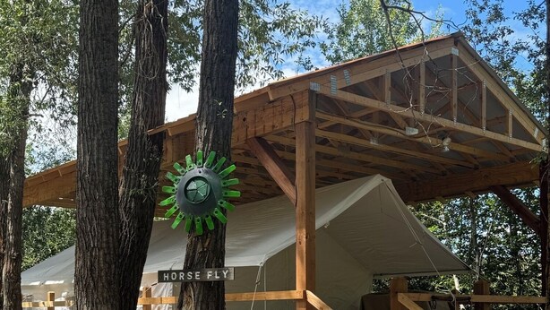 Une cabane rustique en bois, dotée d’un porche couvert, d’un escalier en bois et d’une enseigne sur laquelle on peut lire « MOUCHE À CHEVAL ».