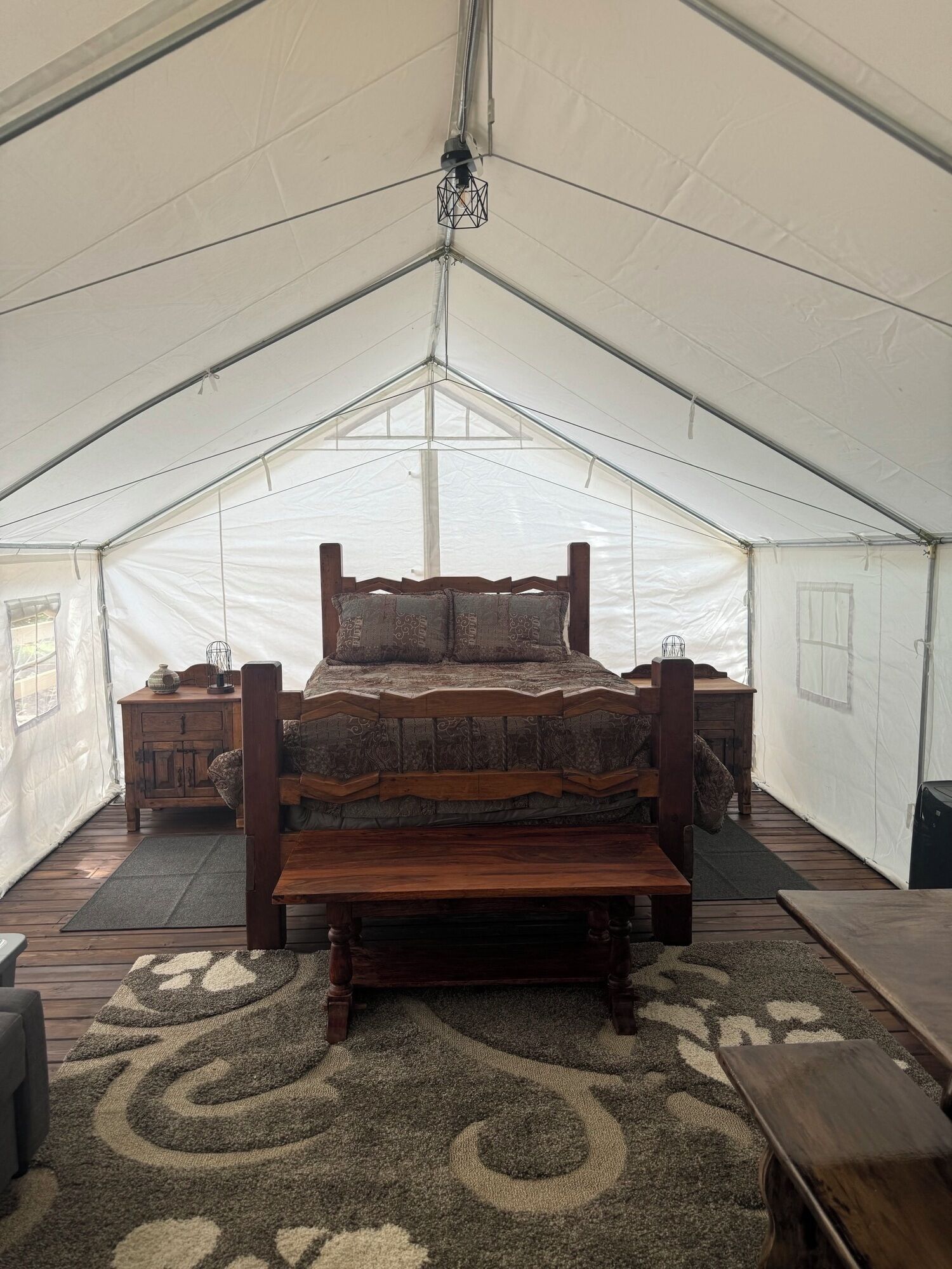 A tented room with a wooden bed, a small table, and a bench.