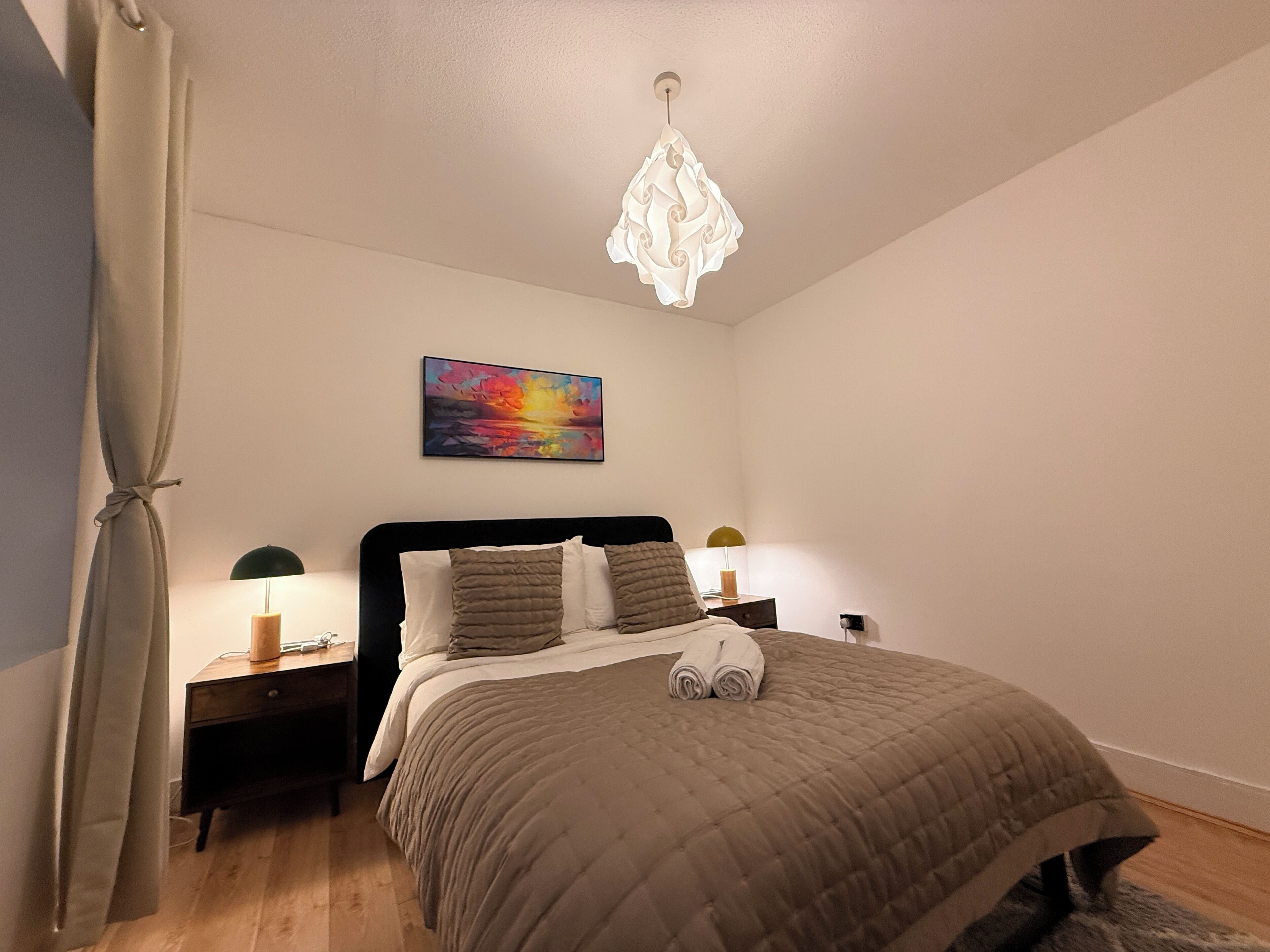Een slaapkamer met een bed, een schilderij, een kroonluchter en bedlampjes.
