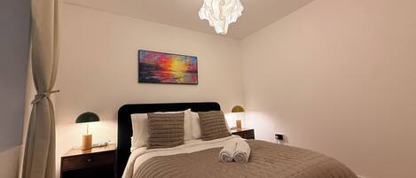 Een slaapkamer met een bed, een schilderij, een kroonluchter en bedlampjes.