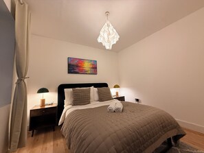 A bedroom with a bed, a painting, a chandelier, and bedside lamps.