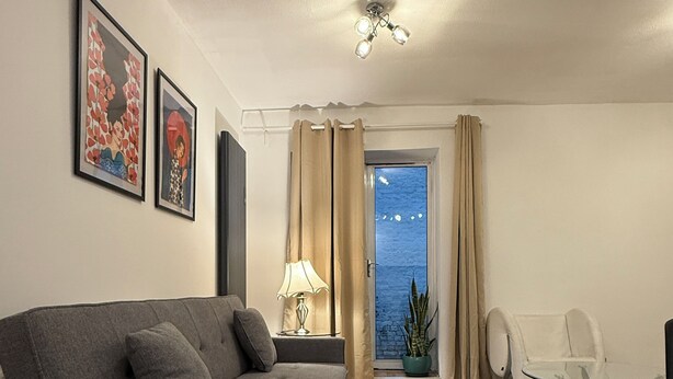 A modern living room with a grey sofa, a glass coffee table, and a view of the sea through a window with curtains.