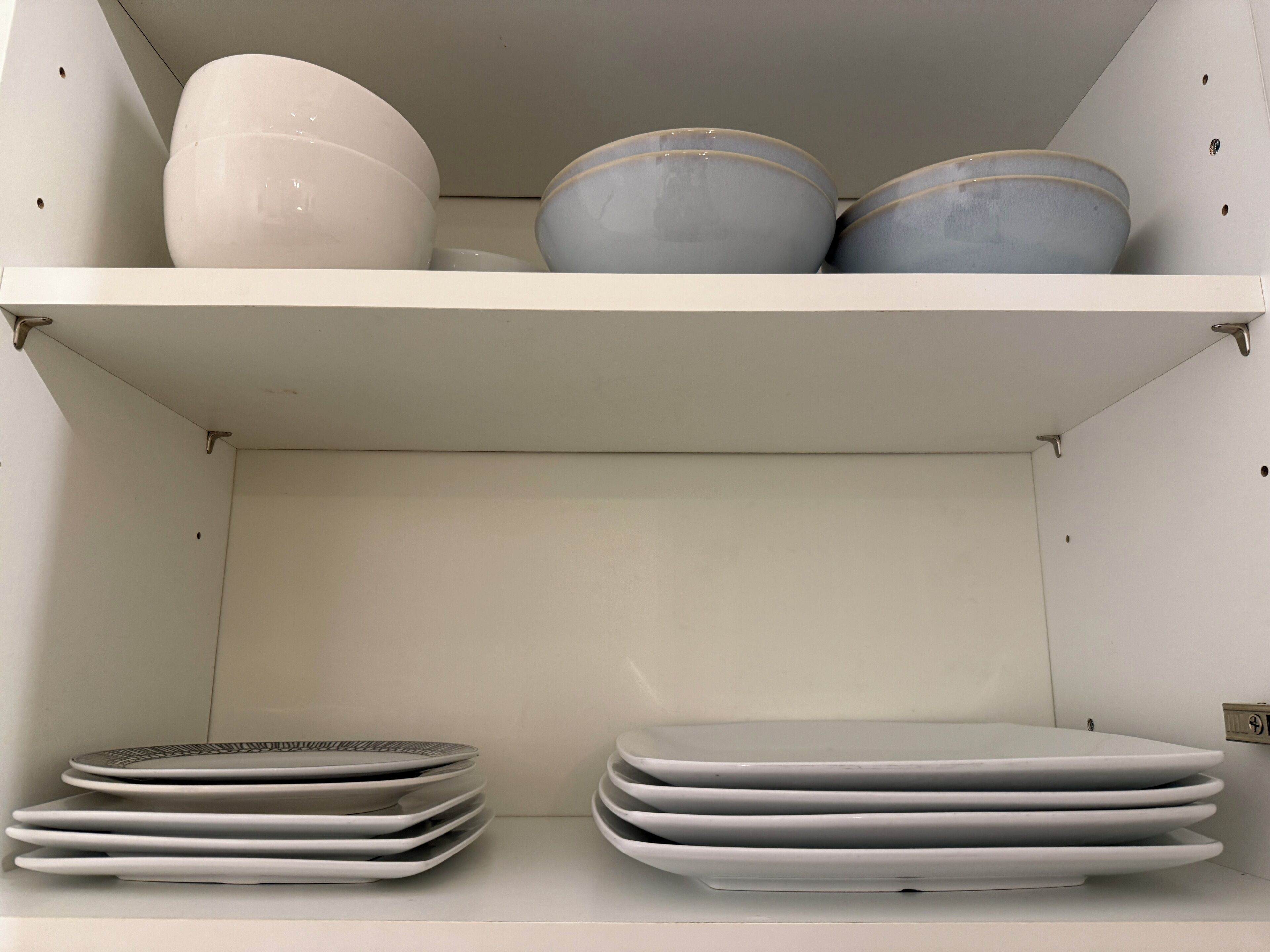 Une étagère blanche avec des bols et des assiettes blancs et gris.