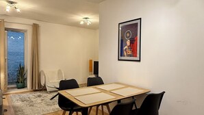 A modern living room with a wooden floor, a dining table with four chairs, a sofa, a TV, and a framed picture on the wall.