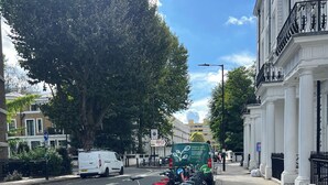 A street with parked bicycles, a white van, and a building with columns.