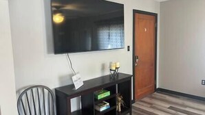 A room with a flat-screen TV mounted on the wall, a wooden door, a dark wooden console table with a few items, and a striped chair. - Rhine Suite at Brickhouse Inn (Hermann)