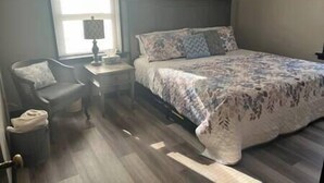 A bedroom with a bed, a chair, a nightstand, and a window. - Rhine Suite at Brickhouse Inn (Hermann)
