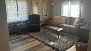 A living room with a patterned rug, a sofa, a chair, a coffee table, and a ceiling fan. - Rhine Suite at Brickhouse Inn (Hermann)