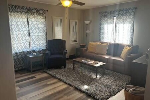 Una sala de estar con un tapete estampado, un sofá, un sillón, una mesa de centro y un ventilador de techo.