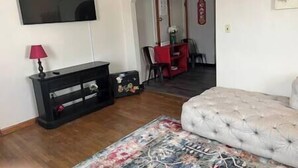 A living room with a flat-screen TV, a red dining table, and a beige sofa. - Roam Suite at Brickhouse Inn (Hermann)
