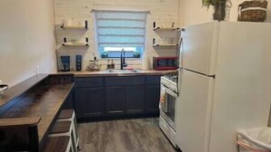 A compact kitchen with dark cabinets, a white refrigerator, and a window above the sink. - Roam Suite at Brickhouse Inn (Hermann)