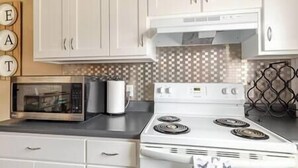 Una cocina con armarios blancos, microondas, estufa y salpicadero de azulejos.