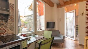 A compact kitchen with a built-in stove, a dining area with a table and chairs, and a TV mounted on the wall. - Aperol in Iseo With 1 Bedrooms and 1 Bathrooms (Iseo)