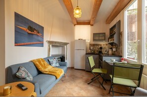A compact living space with a sofa, a small dining table, a kitchen area with a refrigerator, and a window providing natural light. - Aperol in Iseo With 1 Bedrooms and 1 Bathrooms (Iseo)