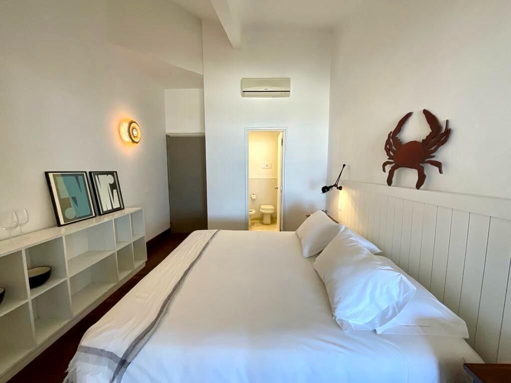 A hotel room with a bed, a bedside table, a wall-mounted light, and a door leading to a bathroom.