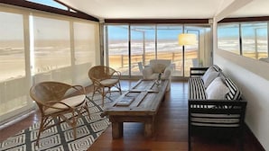 Una stanza con un'ampia finestra vista spiaggia, arredata con un tavolo di legno, sedie e un divano a righe.