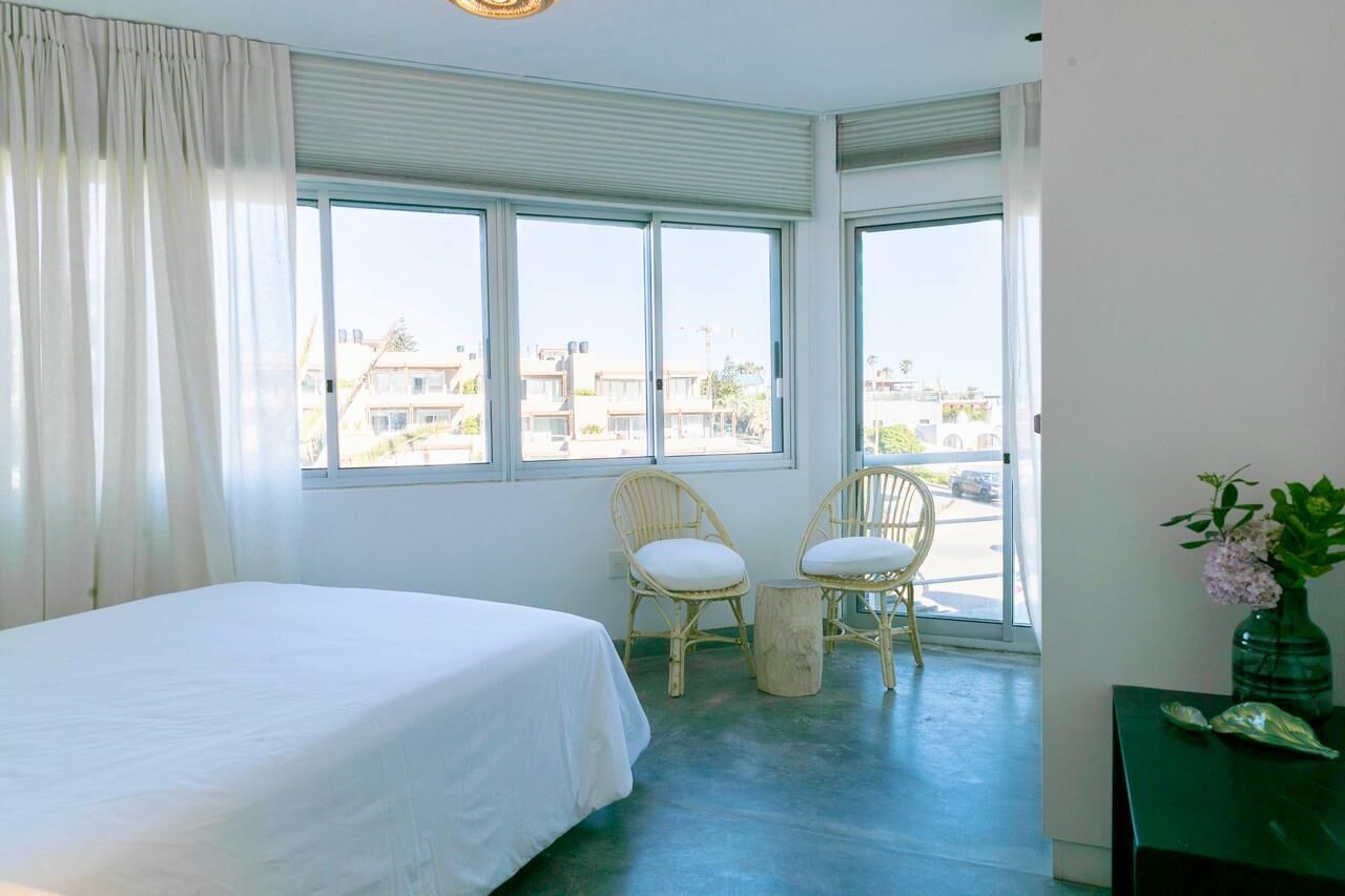 A hotel room with a bed, two chairs, a small table, and a view of the city through large windows.
