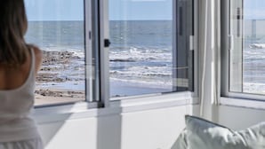Une pièce dotée d’une grande fenêtre donnant sur une plage rocheuse et la mer.