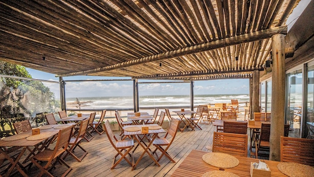 Una terrazza esterna in legno con tavoli e sedie, affacciata sull'oceano.